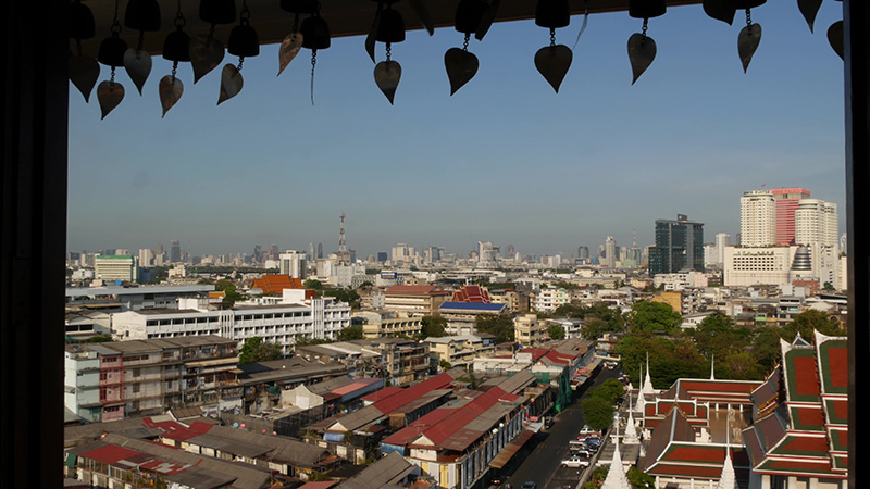 Cityscape of modern oriental town. View from the window of houses roofs on streets of majestic Bangkok from Golden Mount Temple during sunset time. Traditional metal bells with wishes hanging.