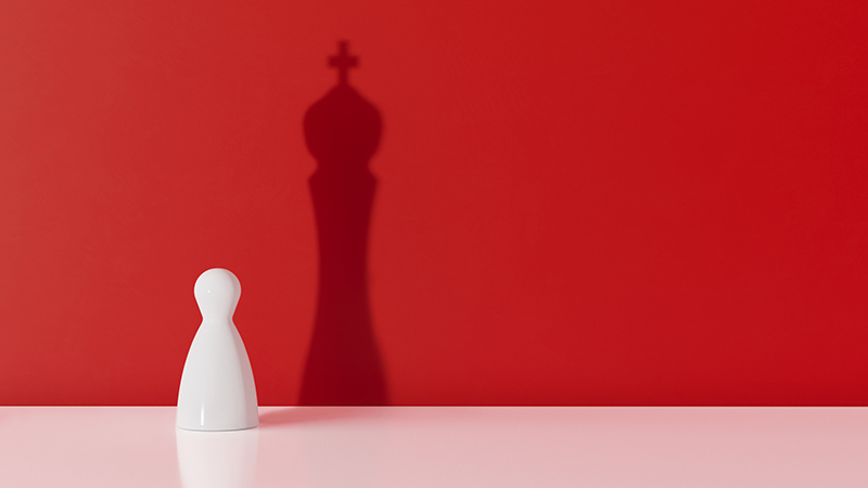 White chess pawn casting the shadow of a king over red background. Leadership and ego concept. Horizontal composition with copy space.