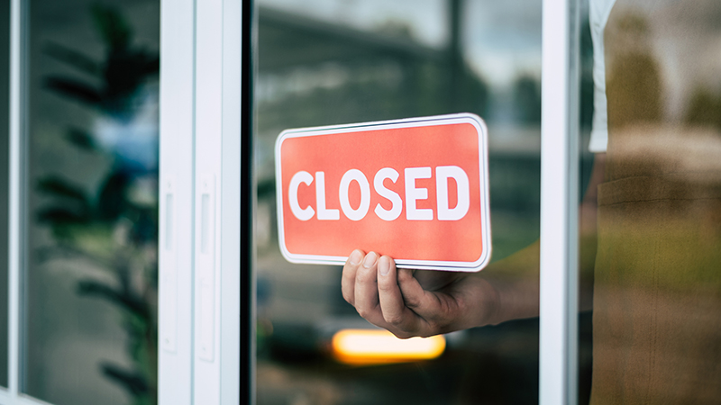 A retail store owner in a coffee shop is seen turning the closed sign on the door's glass surface. The widespread closures of stores, and restaurants during the COVID-19 lockdown and quarantine period