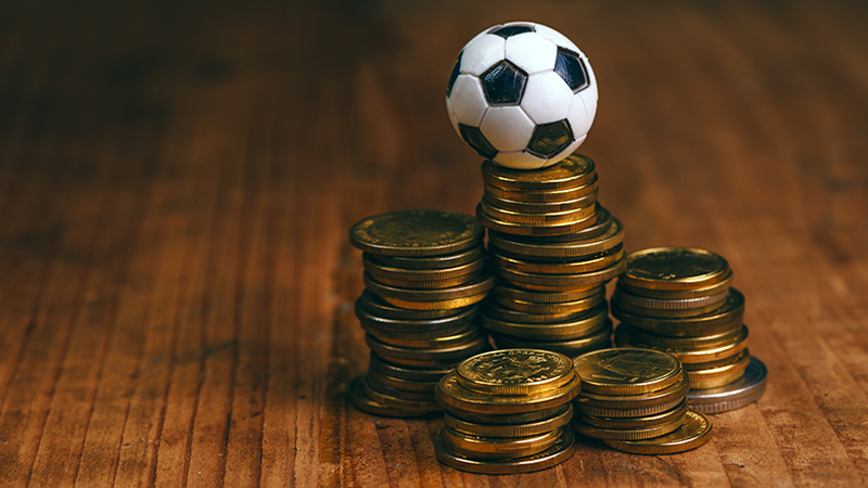 Soccer bet concept with small football on top of coin stack, making money by predicting sport results.