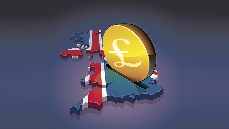 A coin with the symbol of the British pound sterling is inserted into a slot of the United Kingdom 3D map in the colors of the British flag like a piggy bank