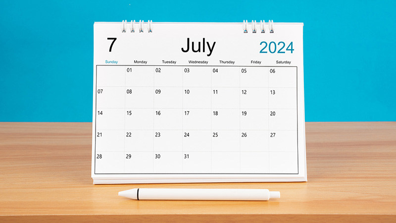 July monthly desk calendar for 2024 year and pen on wooden table with blue color background.