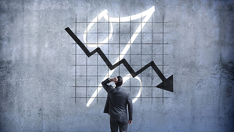 A businessman places his hand on his head as he looks up and is perplexed by a chart indicating falling interest rates.