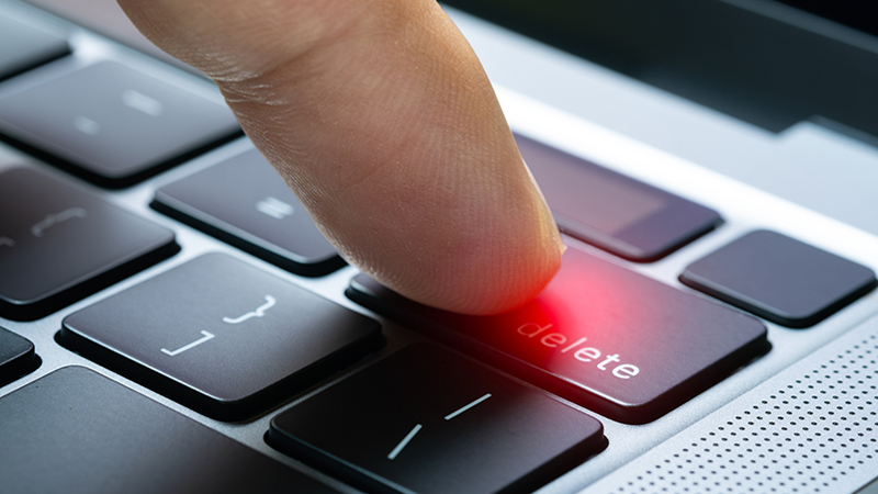 Finger of the computer user, he presses the delete button on the computer keyboard.