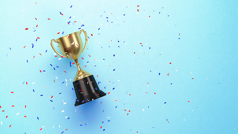 Colorful confetti falling over gold cup sitting over blue background. Horizontal composition with copy space. Directly above.