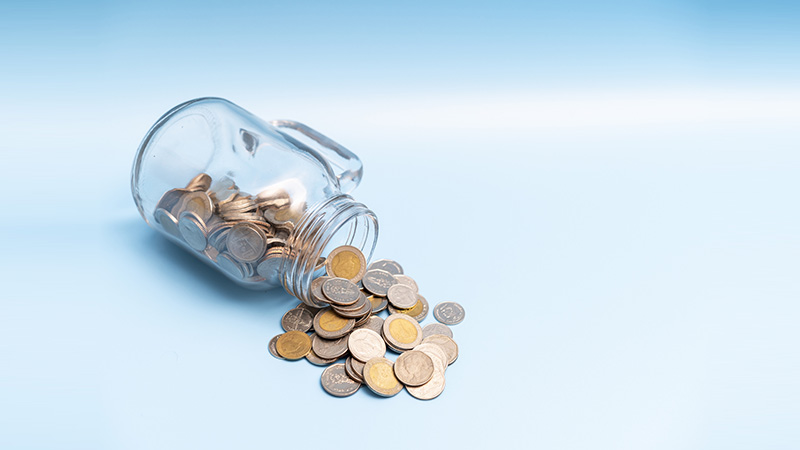 A lot of money coin flow out of the glass jar on blue background, Saving money concept.