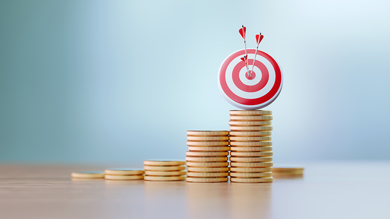 Red dartboard and arrows sitting over coin stacks before defocused background. Horizontal composition with copy space. Success and accuracy concept.