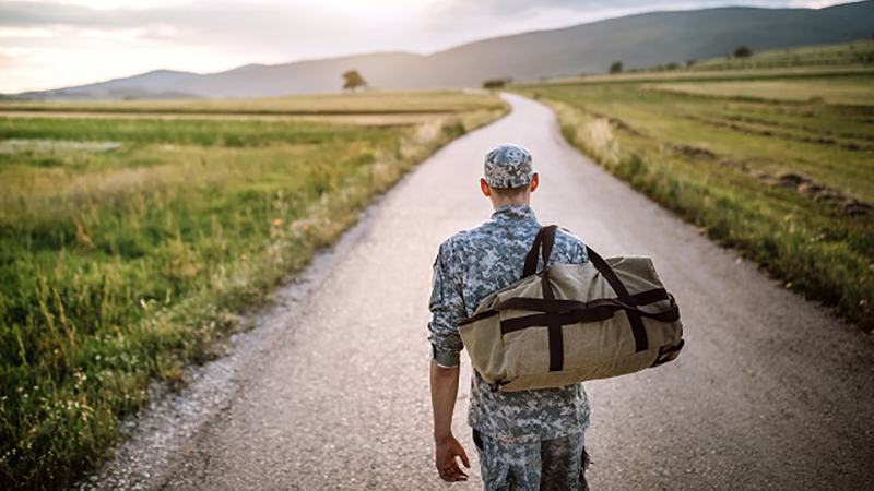 Soldier in army fatigues walks along an empty road